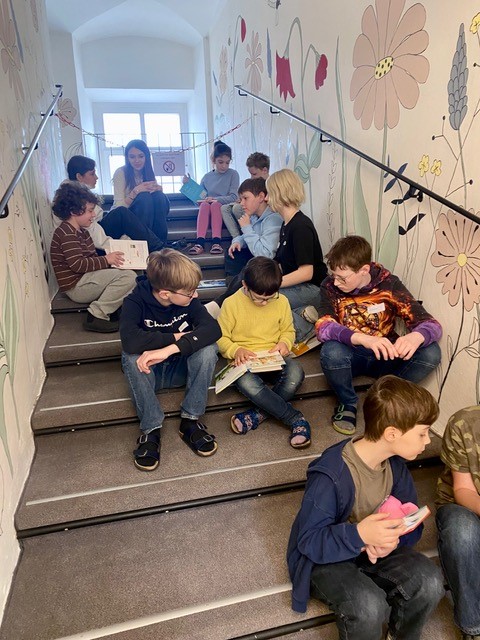 Schülerinnen und Schüler sitzen lesend auf der bunt bemalten Lesetreppe der Bibliothek